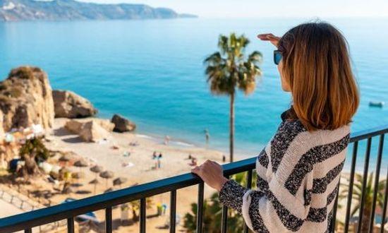Woman standing on a balcony looking over Nerja beach